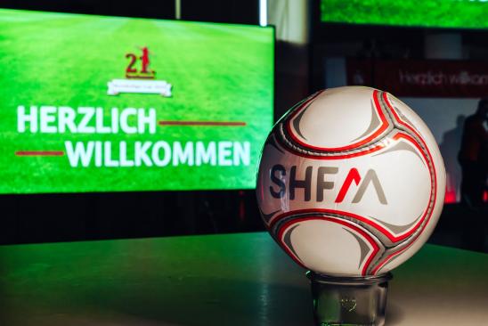 Ball mit SHFM Logo vor Bildschirm mit Schrift Herzlich Willkommen